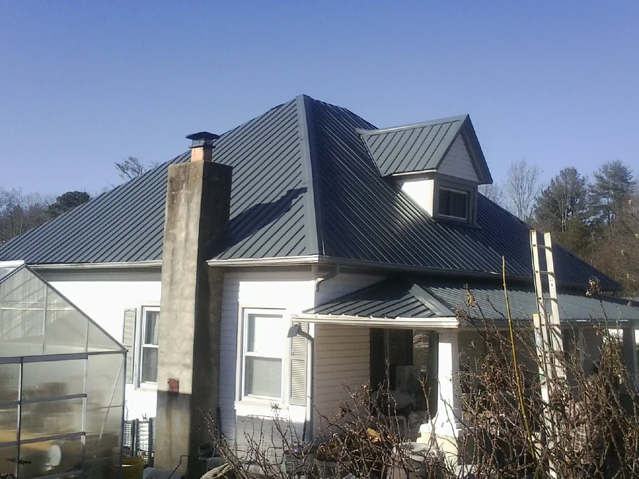Dark blue standing seam metal roof on a white farmhouse with dormer — Slate & Tile Roof Repair by Roofing Brothers in Nobleton