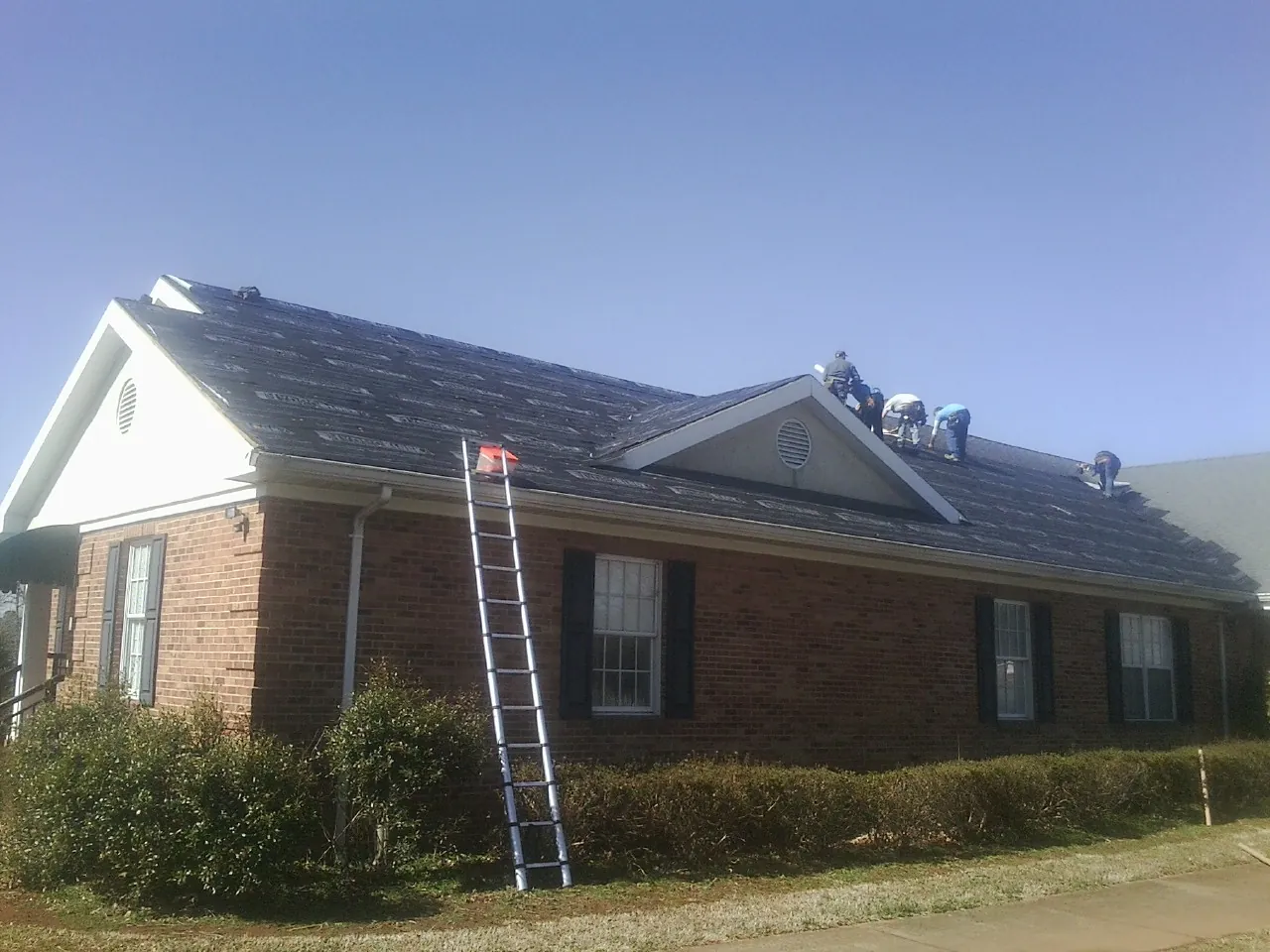Crew tearing shingles off a brick ranch roof with a ladder set — Metal Roof Repair work by our crew in Nobleton