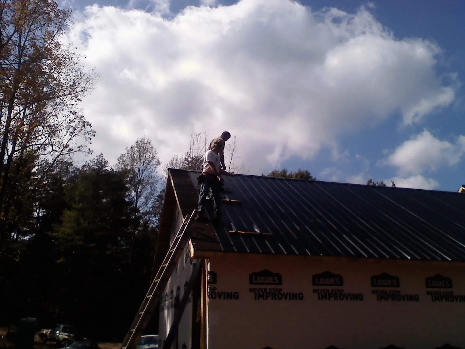 Roofer fastening dark metal panels high against a cloudy sky, from a Roof Inspection job in Nobleton